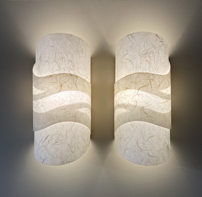 two lit cylinder sconces with cut out waves